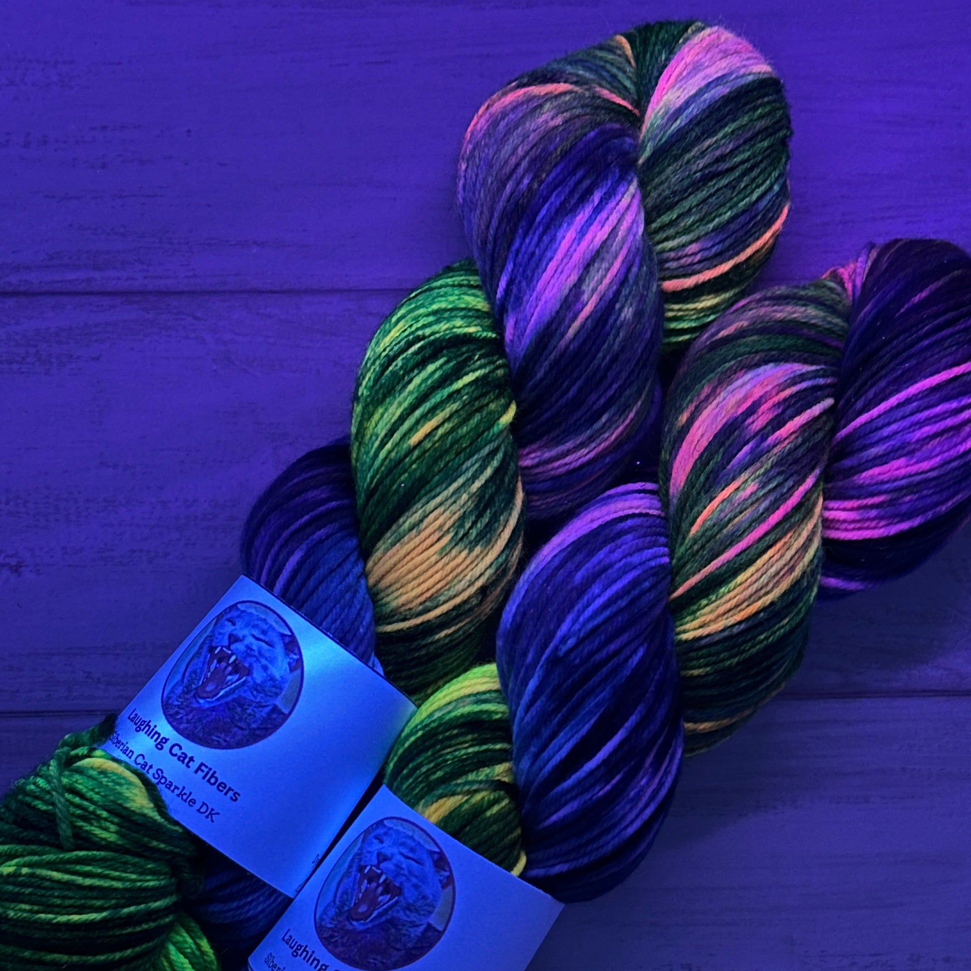 two skeins of sparkle DK hand dyed yarn under black light by Laughing Cat Fibers in their Cartwheel Galaxy colorway 