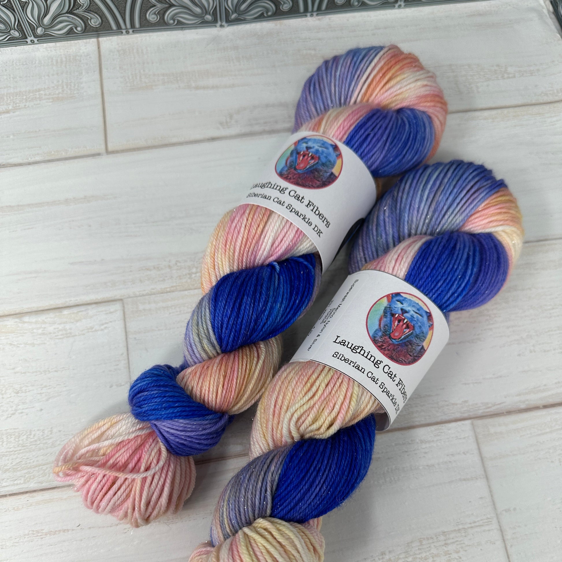 Two skeins of multicolored yarn with labels on a light wooden surface.