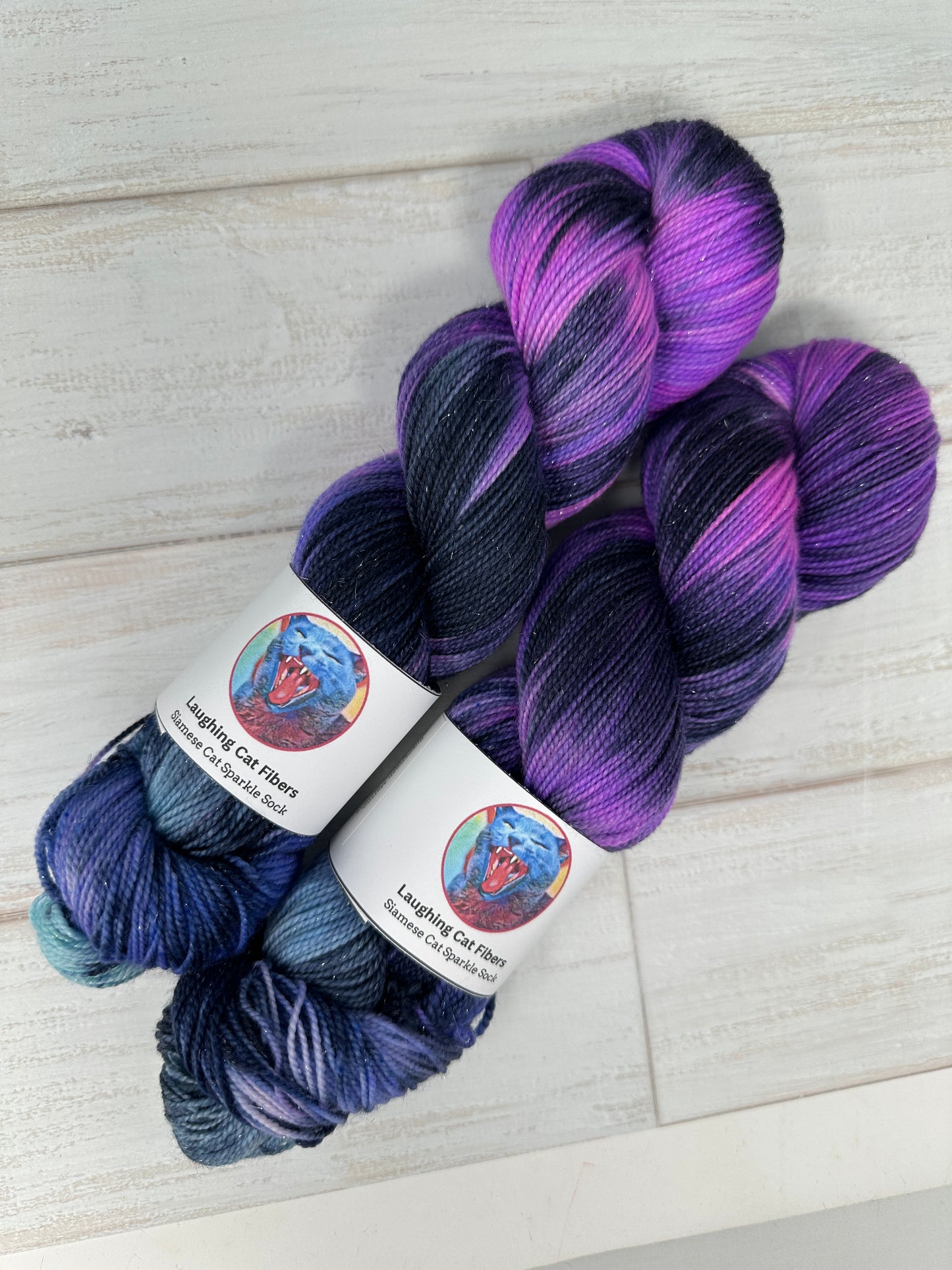 Two skeins of purple and blue yarn with labels on a light wooden surface