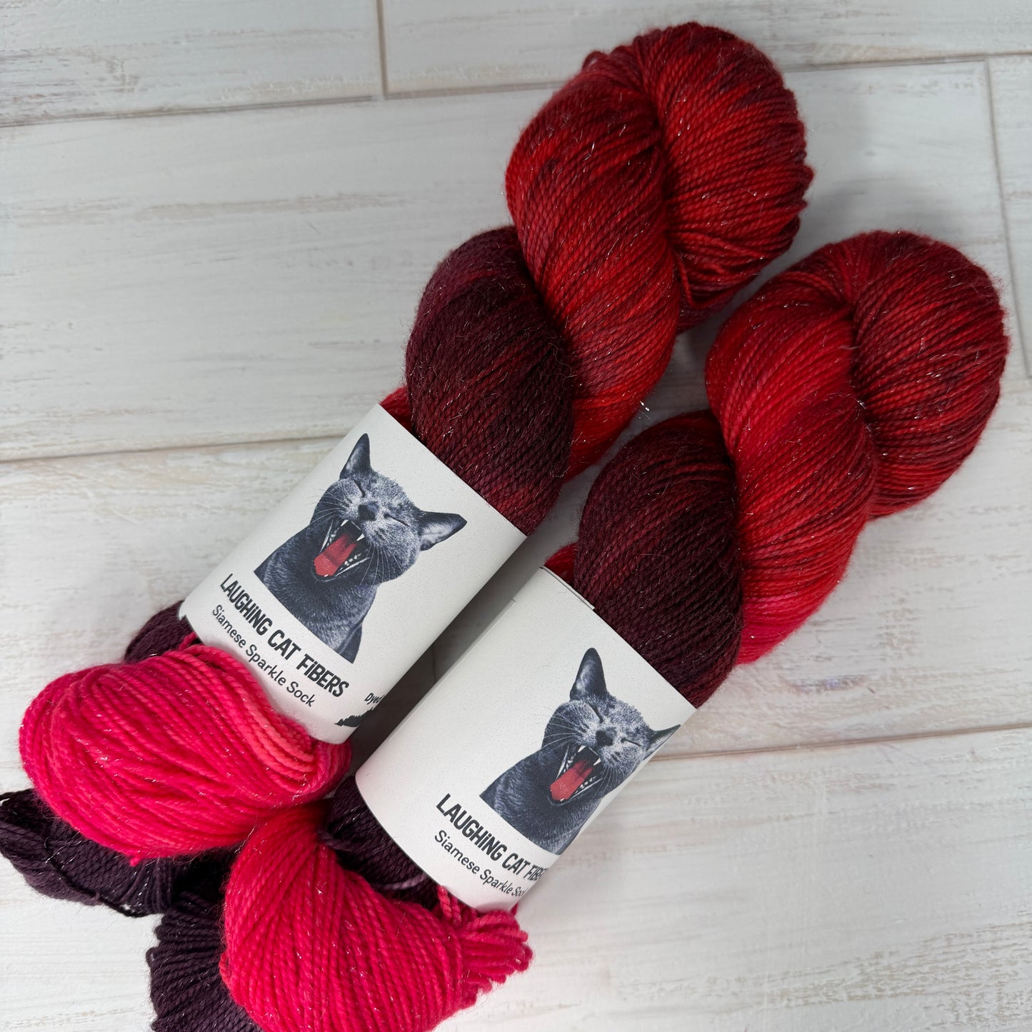 Two skeins of red and pink hand dyed sparkle sock  yarn by Laughing Cat Fibers in their Heart Nebula colorway 