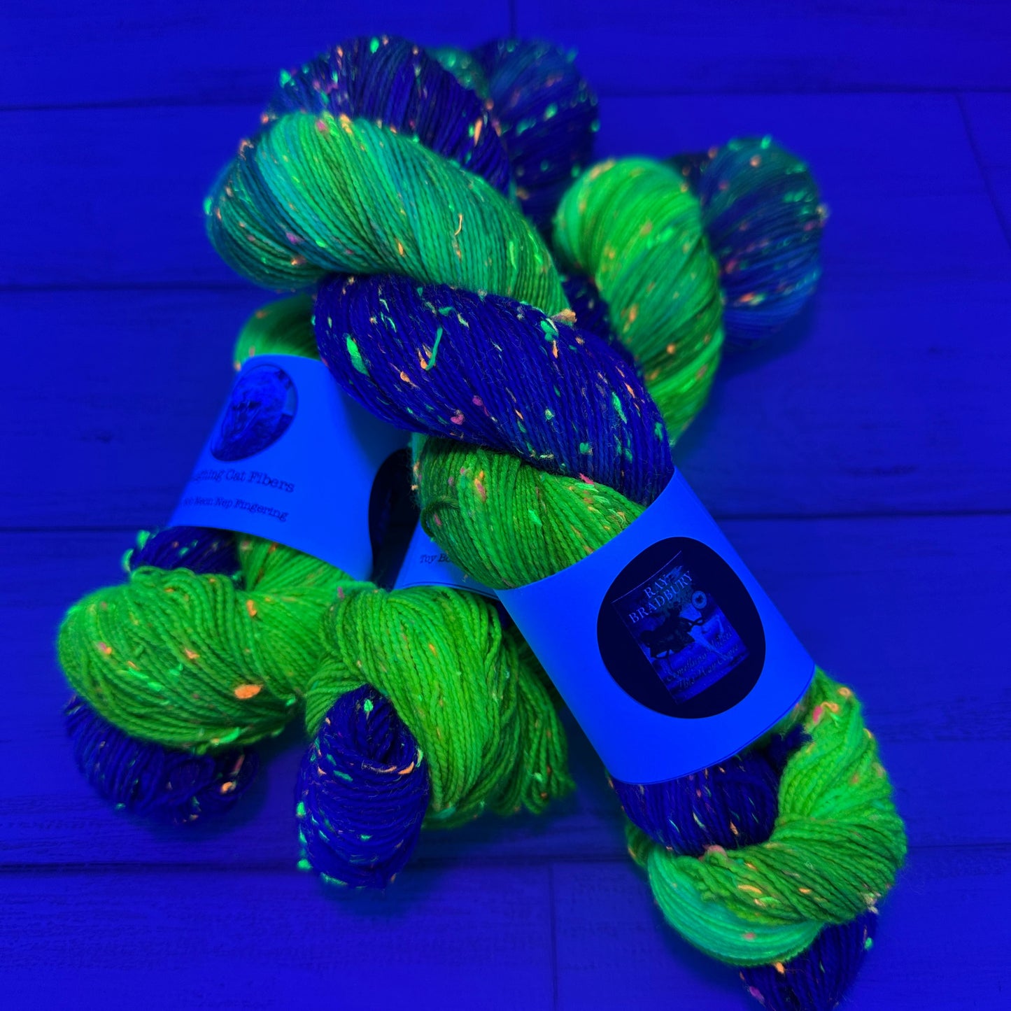 Green and blue yarn skeins on a blue background under black light