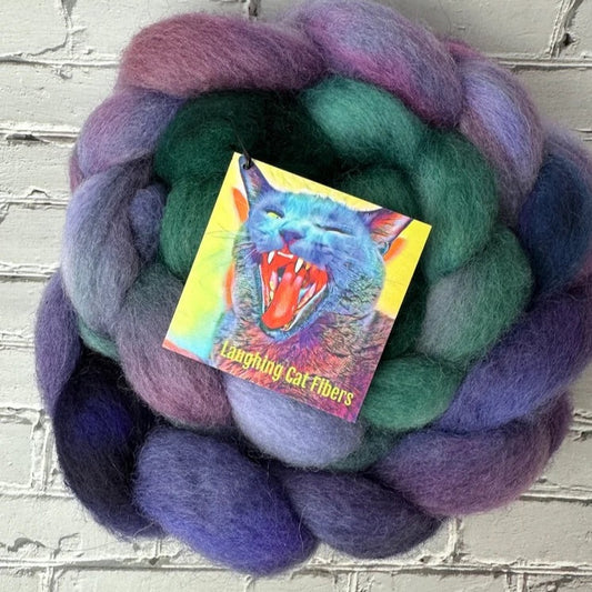 A bundle of multicolored wool roving dyed in various shades with a card showing a graphic of a roaring cat in the center.