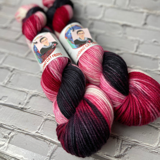 Two skeins of multicolored yarn with labels on a textured gray surface