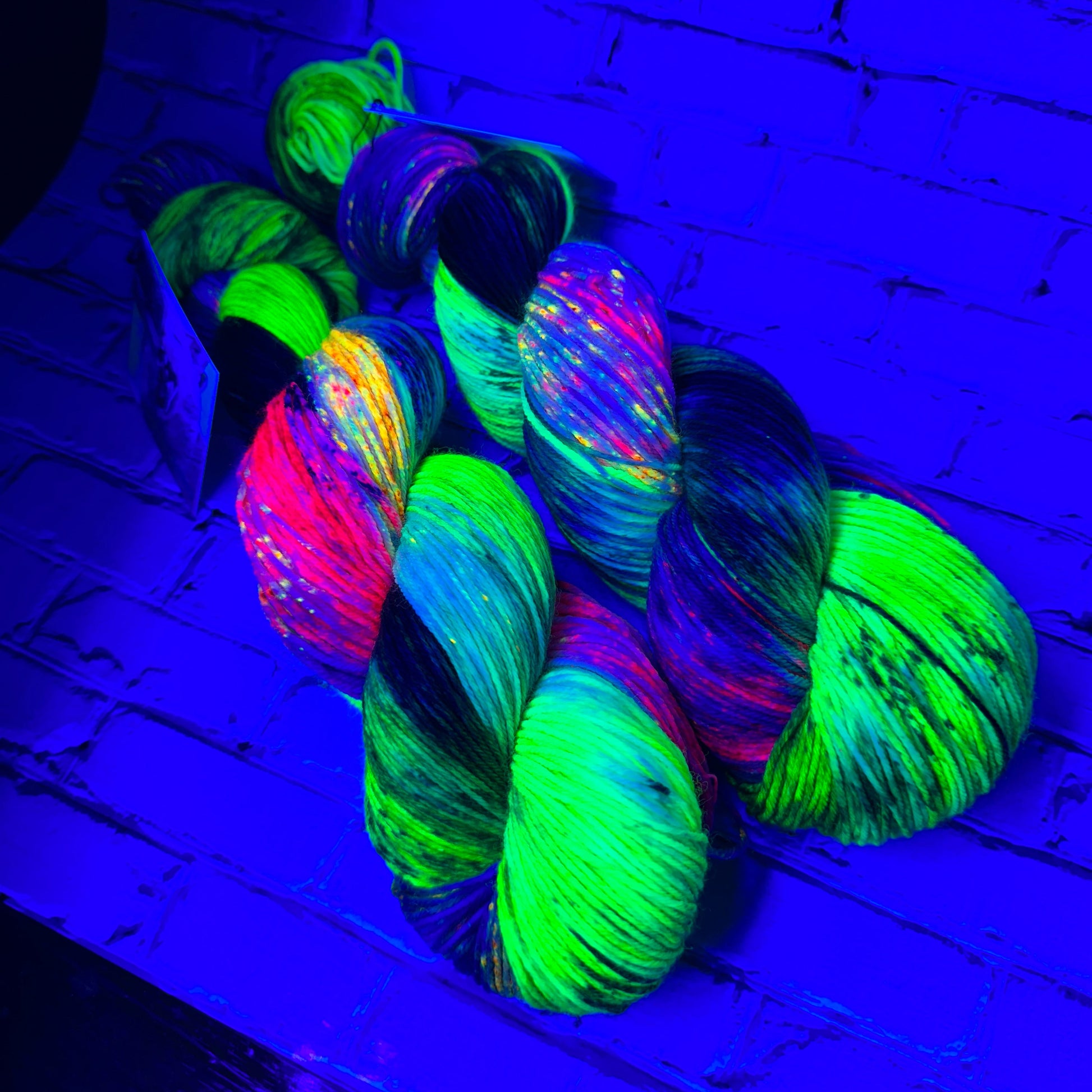 two skeins of Ophelia hand dyed yarn by Laughing Cat Fibers under black light 