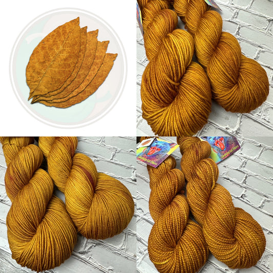 A collection of yarn skeins in a brown color, resembling the appearance of tobacco leaves, displayed on a brick background.